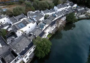 Residential buildings with white plaster walls and clay tile roofs, surrounded by water and greenery.