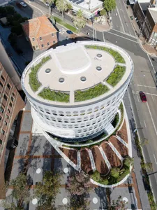Aerial view of a modern building with a green roof surrounded by streets and trees.