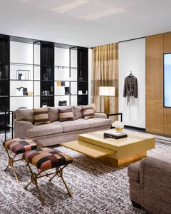 A modern living room featuring a beige couch, yellow coffee table, and glass shelves displaying various fashion items.