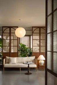 Minimalist living room with beige sofa, wood flooring, and large potted plants.