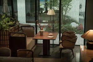 Modern living room with wooden furniture and potted plants, featuring a wooden table with a vase of flowers and a book, and r