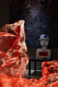 An abstract artwork featuring a red, flowing fabric in the foreground, a stylized figure with a blue hat and a sign reading '