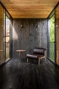 A cozy living space with dark wood walls, floor, and furniture, featuring a modern chair and small side table.