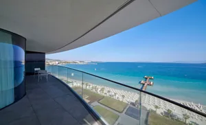 Modern, minimalist apartment balcony overlooking the ocean with clear blue skies and a clear view of the beach.