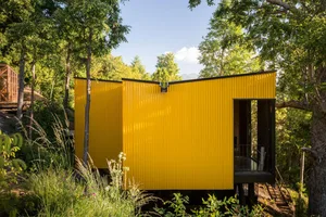 Modern residential studio with a bright yellow corrugated metal exterior nestled in a wooded area.