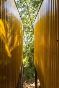A modern exterior featuring bright yellow corrugated metal walls, with trees and the sky visible through the space.