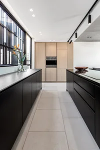 Modern, minimalist kitchen with wooden cabinets, black countertops, and floor-to-ceiling windows.