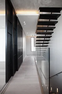 Modern minimalist house featuring a black staircase with glass railings and wooden floors.