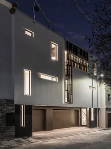 A modern residential building featuring sleek, minimalist design with concrete and glass elements at night.