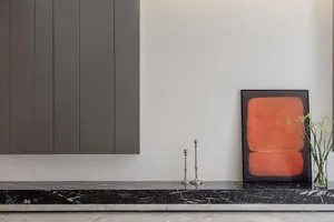 A modern interior scene featuring sleek, dark cabinets, a black marble shelf, and a framed piece of contemporary art with vib