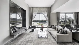 A modern living room with a gray couch, black armchair, glass coffee table, and metallic decorative items.