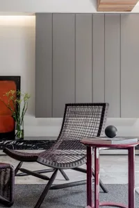 A minimalist living room with a black metal-net chair, a red side table with a black ball and books, and a black marble count