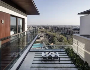 A modern residential outdoor space featuring glass railings, concrete patio, and wooden elements, overlooking a cityscape.