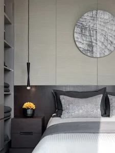 Minimalist bedroom with a bed adorned with gray and black pillows, a white bedspread, and a wooden headboard with metallic el