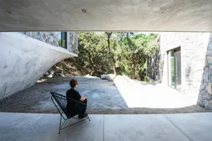 A person sitting in a black chair on a patio overlooking a natural landscape, featuring minimalist architectural design eleme