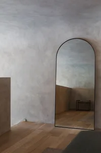 A minimalist interior space featuring a concrete wall with an arched floor mirror.