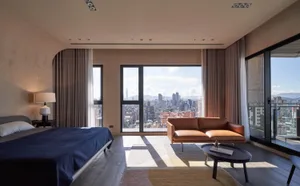 A modern bedroom with a city view, featuring wooden furniture, a large window, and a comfortable sofa.