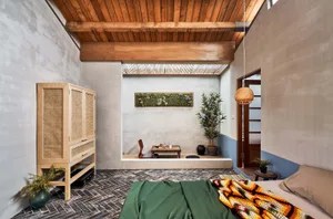 A modern bedroom with a concrete wall, wooden ceiling, and a cozy seating area.