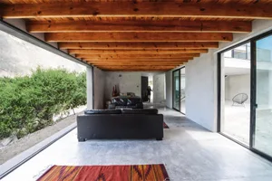 Interior view of a modern living room with concrete flooring, wooden ceiling beams, and black sofas.