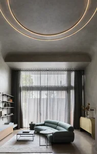 A modern minimalist living room featuring a light concrete ceiling and floor, a sleek green sofa, and a transparent curtain w