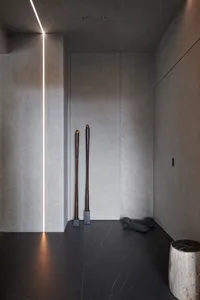 A minimalist interior with concrete walls, black marble floor, and a dark wooden sculpture.