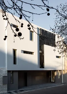A modern residential building with concrete facade, black metal accents, and large windows.