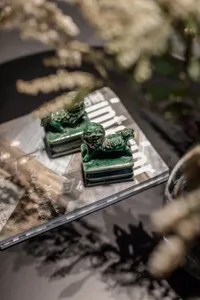 Two green ceramic lion statues on a metallic glass table.