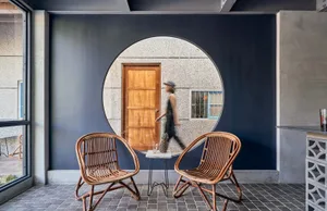 A circular window in a blue wall with a wooden door and woven chairs.