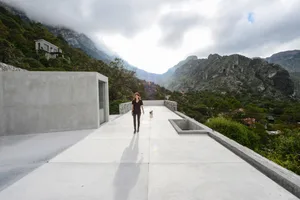 A woman walking her dog on a modern rooftop with concrete flooring and a mountainous landscape in the background.