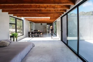 A modern industrial bedroom with concrete flooring and exposed wooden beams on the ceiling.