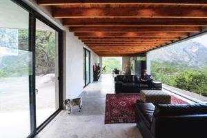 A modern living room with concrete flooring, black sofas, and a wooden ceiling with exposed beams.