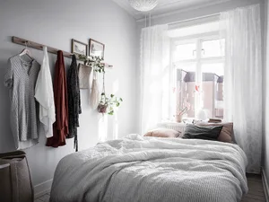 A minimalist bedroom with hanging textiles and a window with a lace curtain.