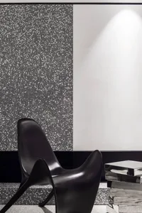 Minimalist black chair against a speckled terrazzo wall and a white wall, illuminated by ambient lighting.