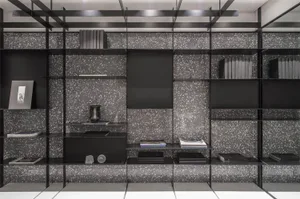 A modern metal bookshelf with black shelves and speckled black and white background.