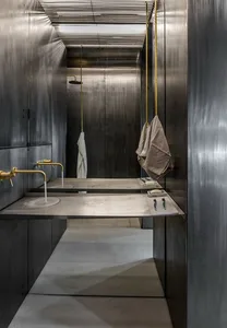 A minimalist industrial bathroom with metallic surfaces, a concrete floor, and hanging towels.