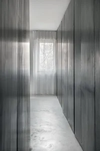 A minimalist residential corridor with metal panels, glass window, and white flooring.
