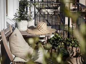 A cozy outdoor space featuring concrete planters, a woven basket, a wide-brimmed hat, and various potted plants.