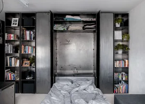 A minimalist bedroom featuring a metallic murphy bed, built-in shelves, and a cozy atmosphere.