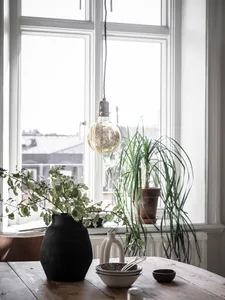 A minimalist interior design featuring wood, ceramic, and cement elements, including a potted plant, hanging lightbulb, and d