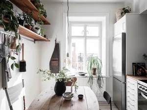 A minimalist kitchen featuring a wooden countertop, metal sink, and glass vase with greenery.