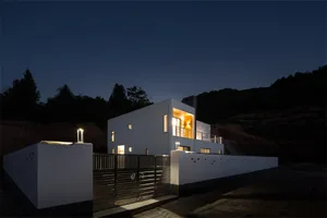 Modern house with concrete exterior illuminated at night, featuring a unique architectural design.
