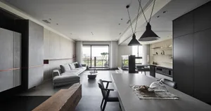 Modern, minimalist living room with concrete walls, a large sectional sofa, and a dining table with pendant lights.