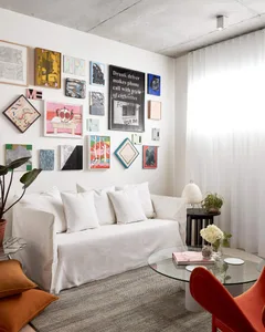 A modern living room featuring a white couch adorned with various framed artworks on the wall, a glass coffee table, and an o