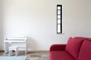 Modern living room with a red sofa, white piano, and wooden flooring.