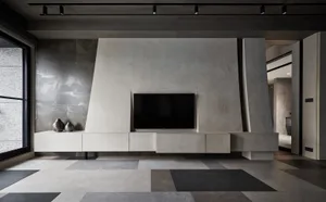 Modern minimalist living room with textured concrete walls and floor, featuring a sleek black flat-screen television.