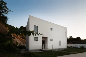 A modern minimalist white concrete residential exterior with cut-out windows, showcasing contemporary architectural design.