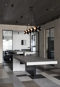 Contemporary office space featuring large concrete tables with black pendant lights hanging from a dark wooden ceiling.