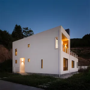 A modern white box-shaped building with concrete exterior at night, featuring small windows and a warm interior light.