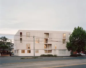 A modern residential building with a white cement façade, featuring large windows and balconies.
