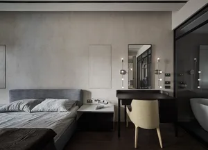 Minimalist bedroom with neutral tones and black furniture, featuring a bed, a desk, and a bathroom in the background.